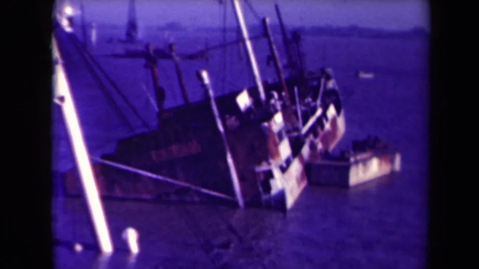 1945 8mm footage from France showing a large listing shipwreck with exposed masts, rigging, and surrounding water.