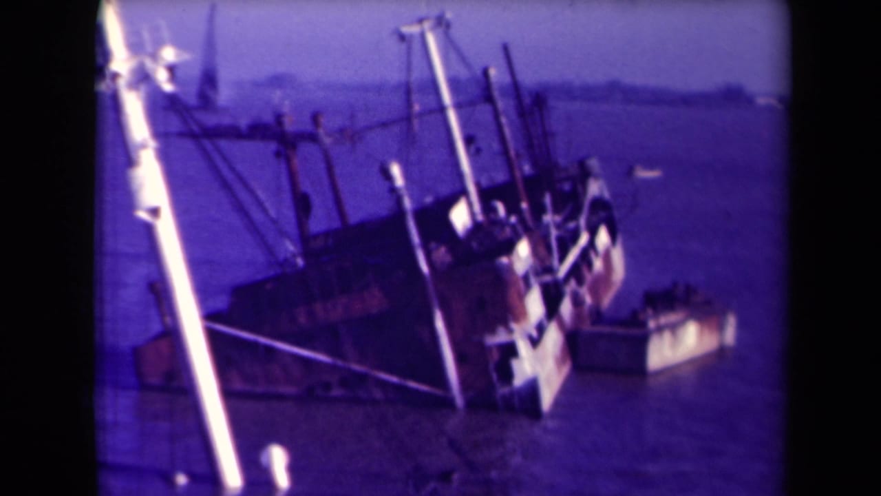 Partly submerged shipwreck viewed from above, with rigging and a small boat nearby.