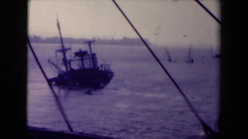 A small vessel moves or sits on French water near visible rigging lines, with a hazy shoreline in the background.