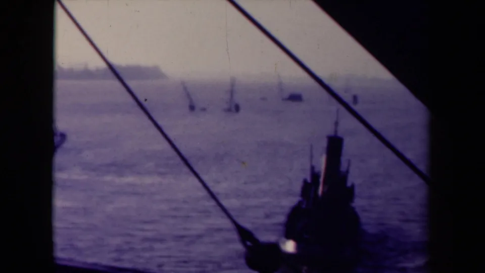 1945 France 8mm frame showing hazy open water, small distant floating forms, a shoreline band, and silhouetted ship structure.
