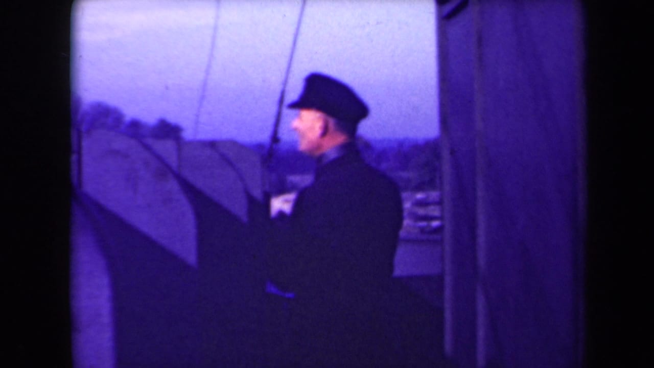 Uniformed man standing on a ship deck near dark ship structure.