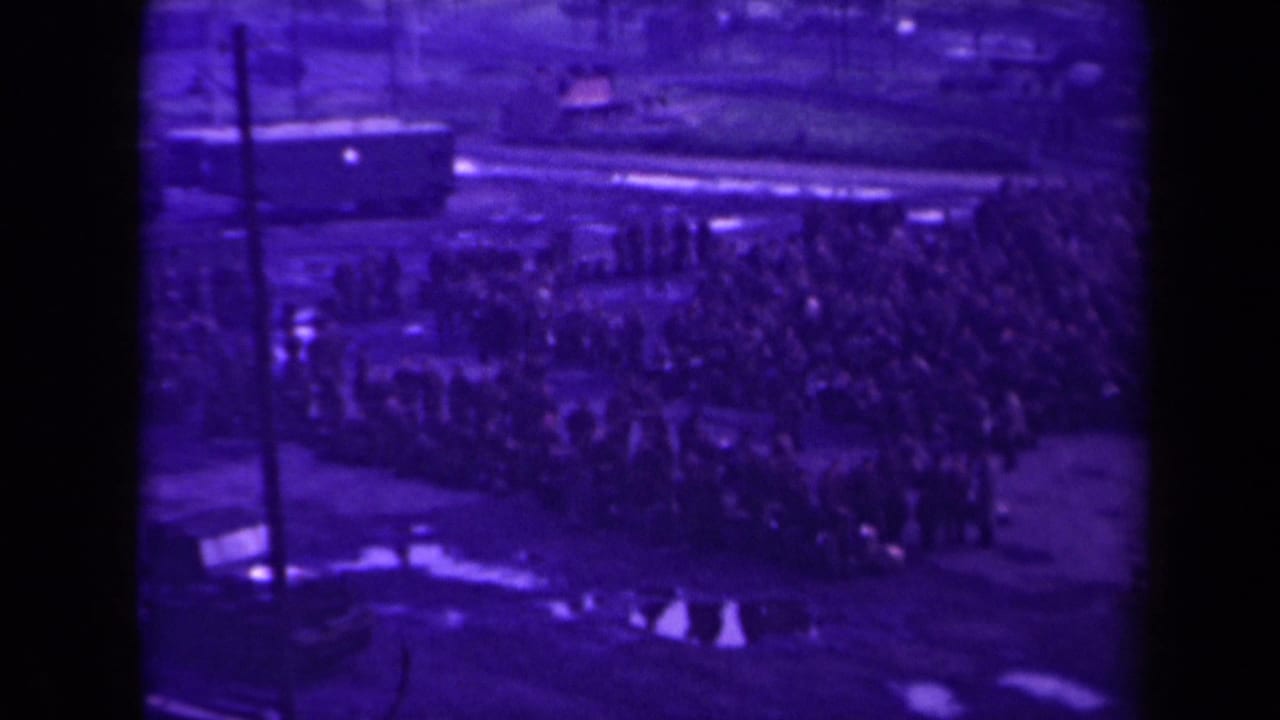 Crowd lined up beside a rail-side area, with a vehicle or train car visible in the background.