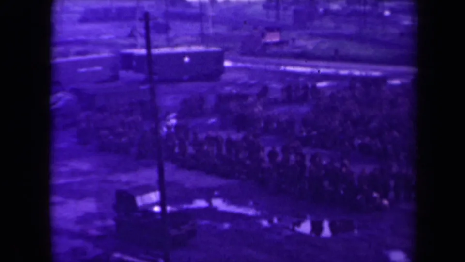 A softer frame shows the same outdoor crowd in metadata-supported 1945 France, with people gathered near poles, puddles, and a rail-side vehicle.