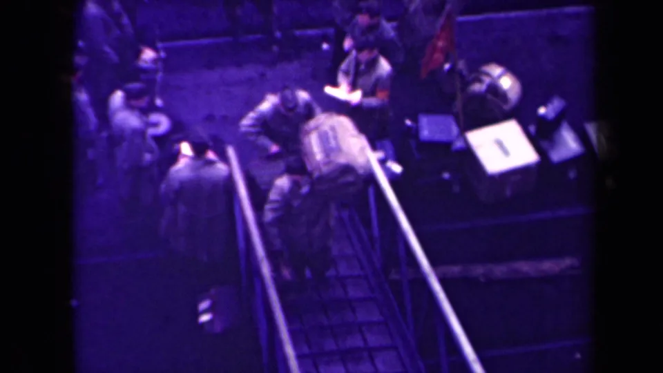 From above, several people in coats or uniforms stand by a stairway or platform area in 1945 France, with bags and nearby equipment visible.