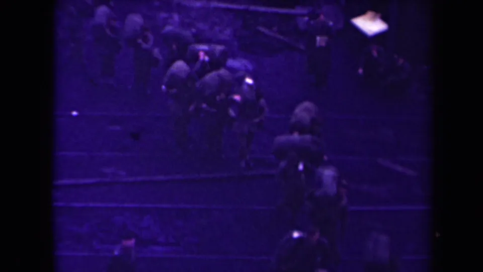 Purple-tinted 1945 France home-movie frame with people viewed from above, many carrying bags or bundles.