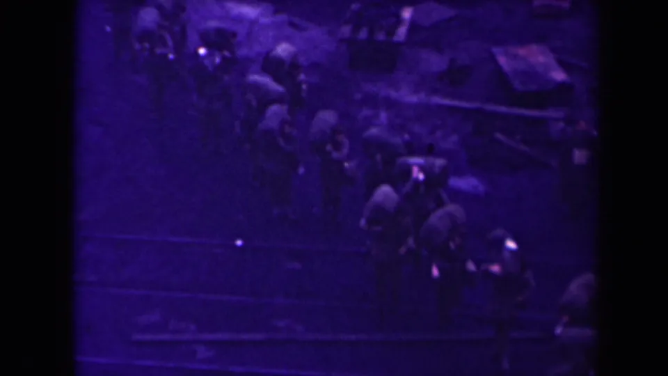 High-angle 8mm frame from 1945 France showing people with packs moving along a dark outdoor route.