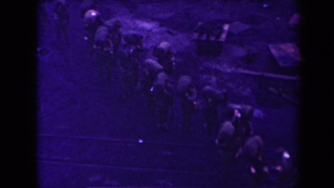 Purple-tinted 1945 France 8mm frame showing a distant group moving in formation across muddy ground near tracks.