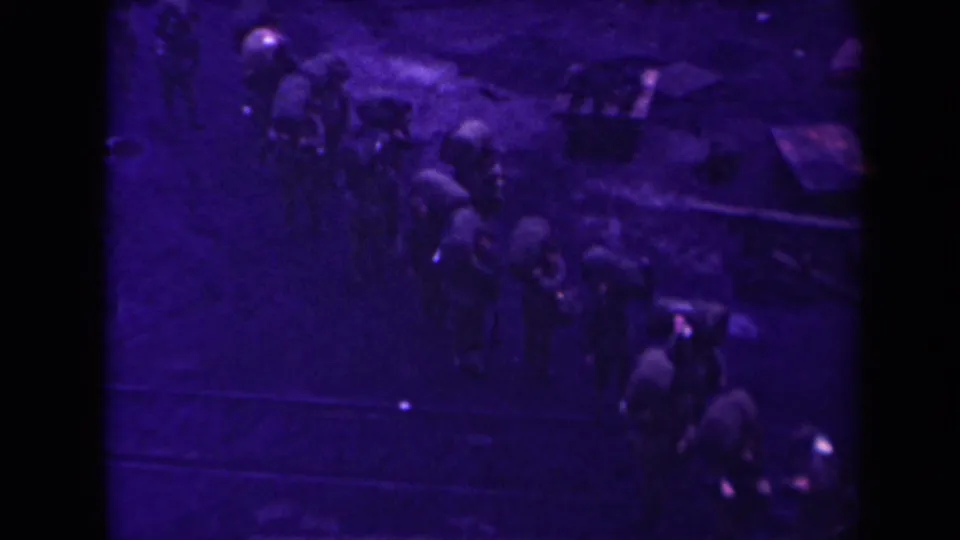Purple-tinted 1945 France 8mm frame showing a distant group moving in formation across muddy ground near tracks.