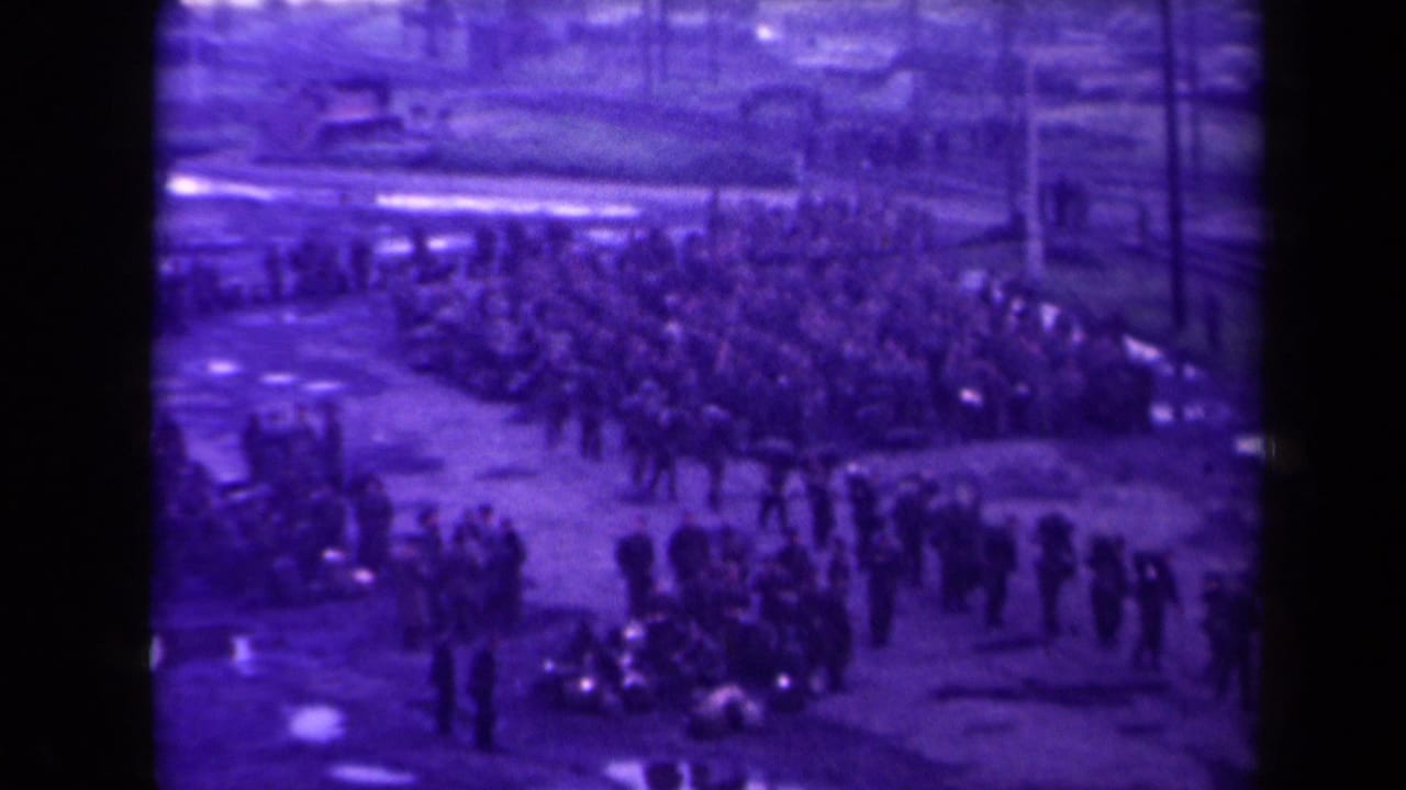Crowd of uniformed soldiers gathered at a dockside near water and industrial structures.