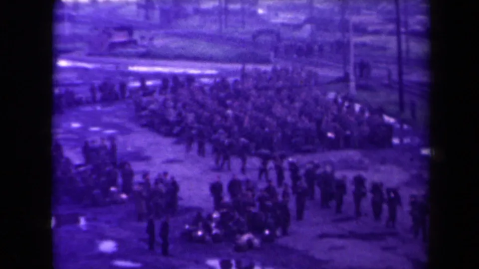 In France according to metadata, uniformed soldiers gather across a quay in grainy purple-tinted 8mm footage.