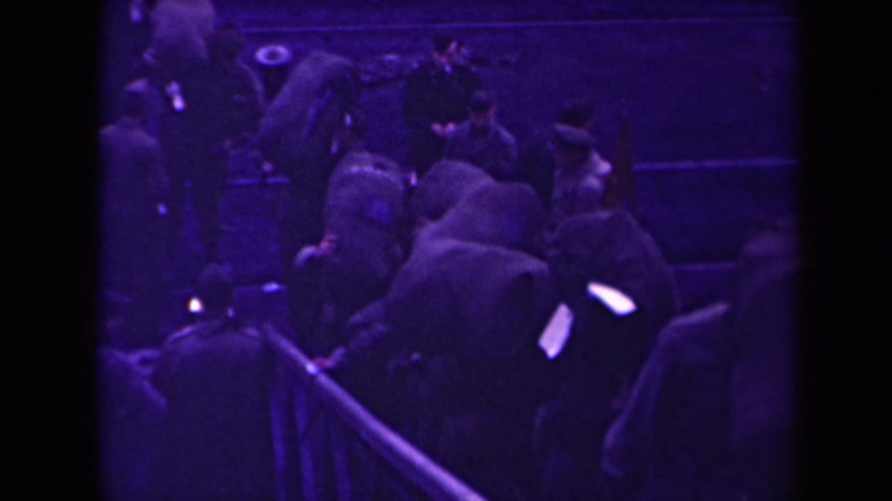 Uniformed soldiers crowd around a gangway beside a dark vessel or dock wall.