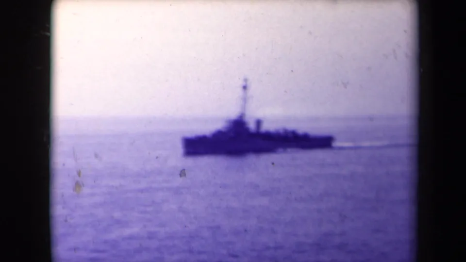 A warship appears in silhouette on calm water, closing the clip with a distant seaward view.