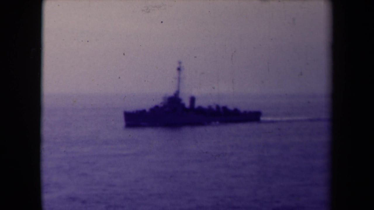 Naval ship in profile on open water with a visible wake.
