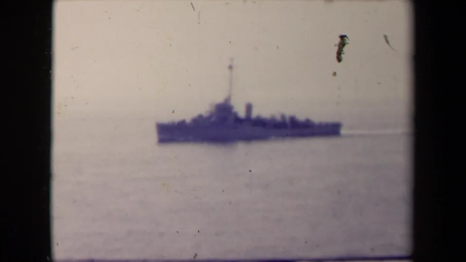 A dark ship remains visible in soft focus on the water, with pronounced scratches, dust, and faded color in the 8mm frame.