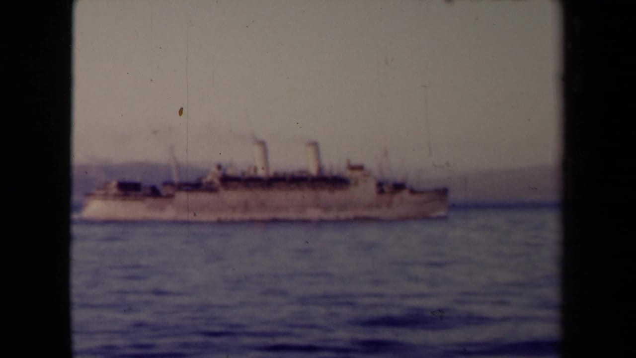 Steamship on calm water with a distant shoreline and hazy sky.
