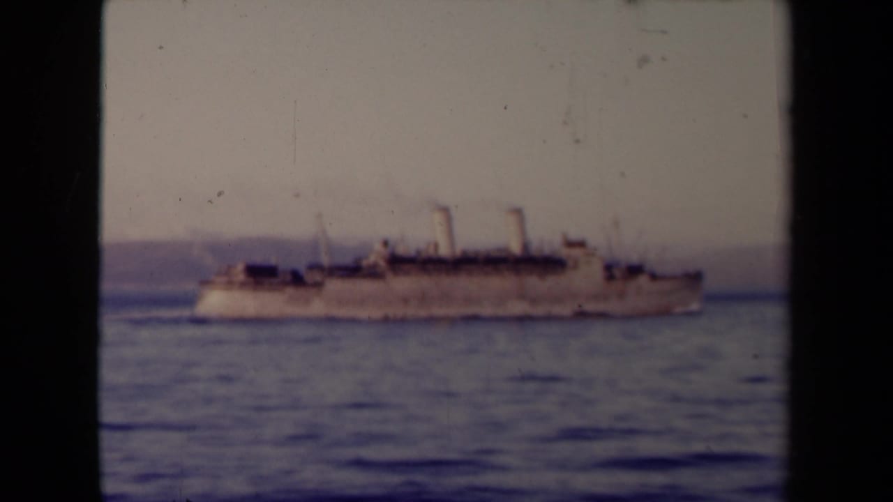 Twin-funnel steamship crossing calm sea before a distant coast.