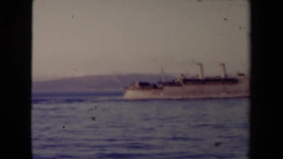 The steamship moves toward the right edge of the 8mm frame, leaving a faint wake across calm water with shoreline still visible behind.