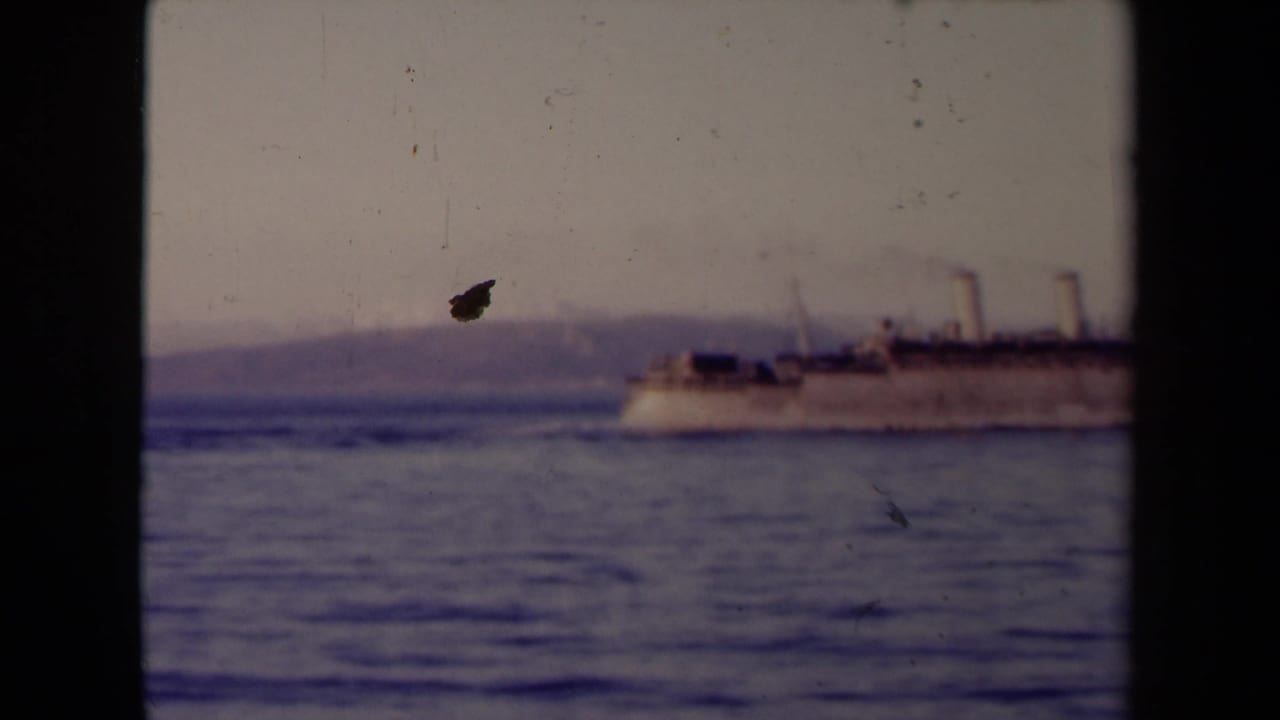 Distant steamship moving across calm water with hazy coastline behind it.