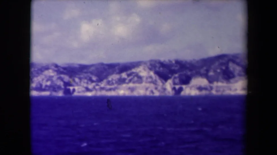 Wide 8mm view of the Marseille seacoast, showing dark blue water, pale shoreline cliffs, and low mountains.