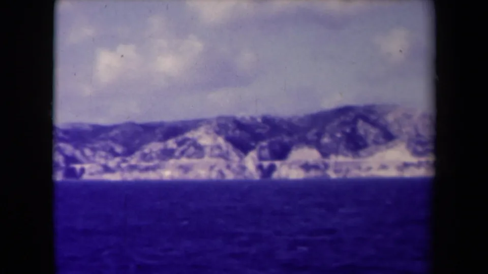 Final frame holds on the Marseille coastal landscape, with textured sea, rocky shoreline, and low mountains under clouds.