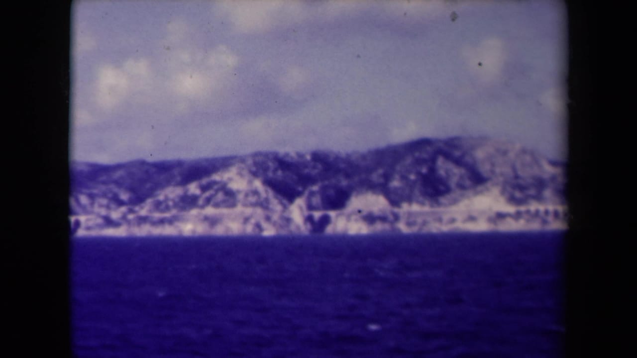 Mountain range across dark blue water under a cloudy sky.