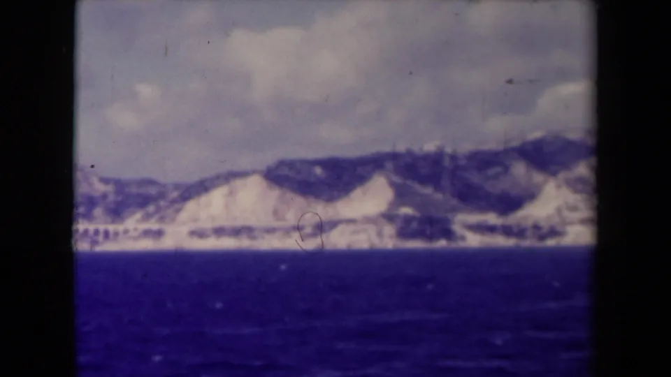 1945 8mm home-movie frame showing a French mountain shoreline across dark water, with grain, dust, and color fading visible in the scan.