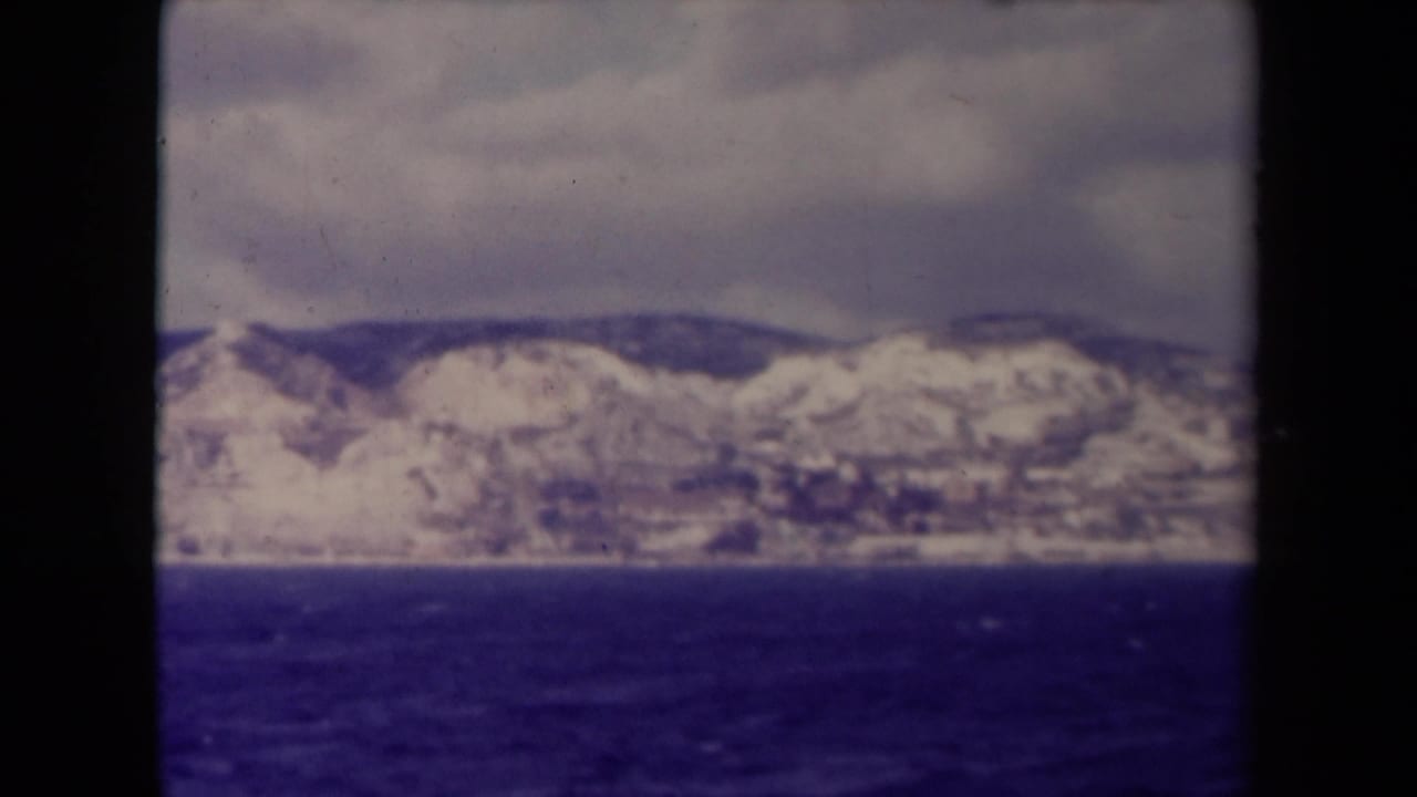 Distant snow-covered mountains across dark water under a cloudy sky.