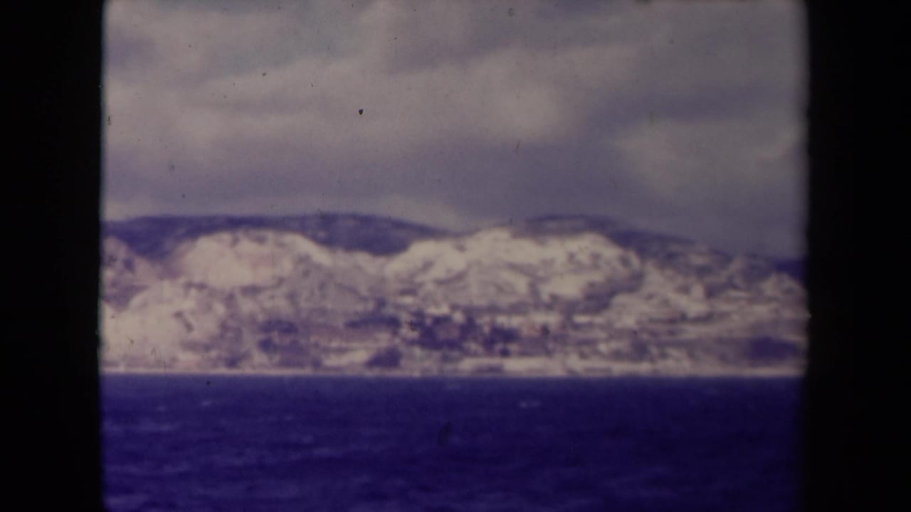 Soft distant mountain ridge with snow above a dark body of water.
