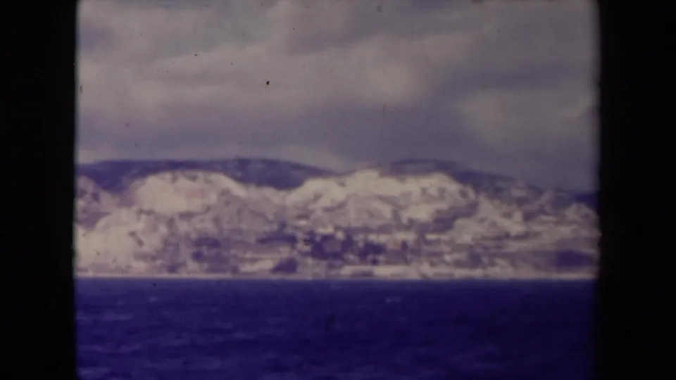 1945 France 8mm view of a snowy ridge and shoreline across dark water, with cloudy sky and faded color.