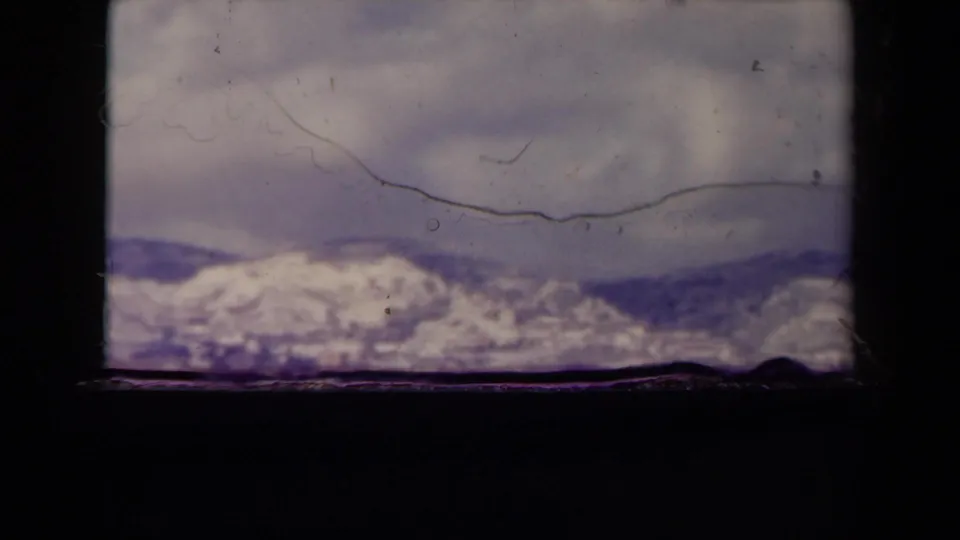 1945 France 8mm frame showing a snowy coastal ridge across water, with film scratches and heavy frame borders visible.