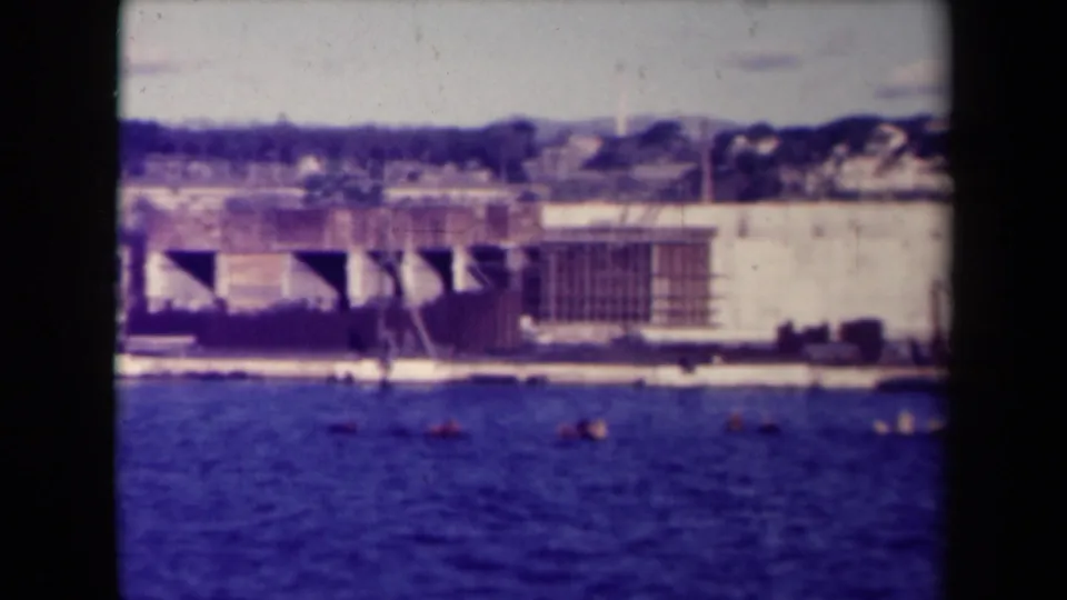 Distant view in France of a large concrete waterfront facility across blue water, possibly a submarine pen.