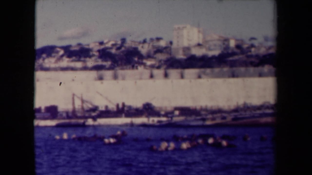 Distant cargo ships and quay wall across blue harbor water.