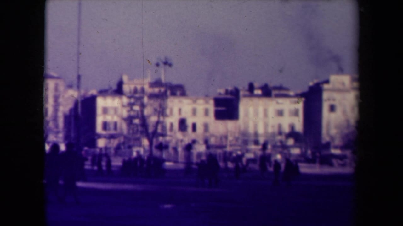 Street scene with buildings, pedestrians, trees, and traffic in the distance.