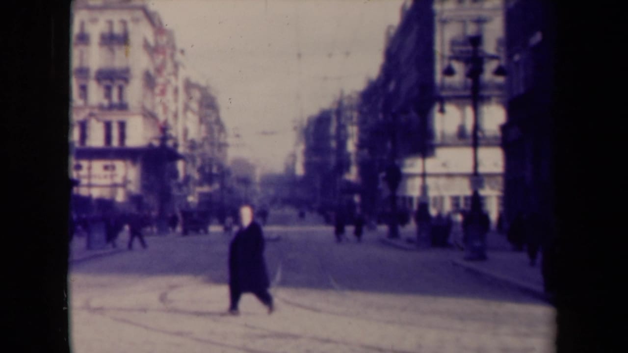 1940s French city street with one foreground pedestrian crossing and distant figures near the sidewalks and building fronts.