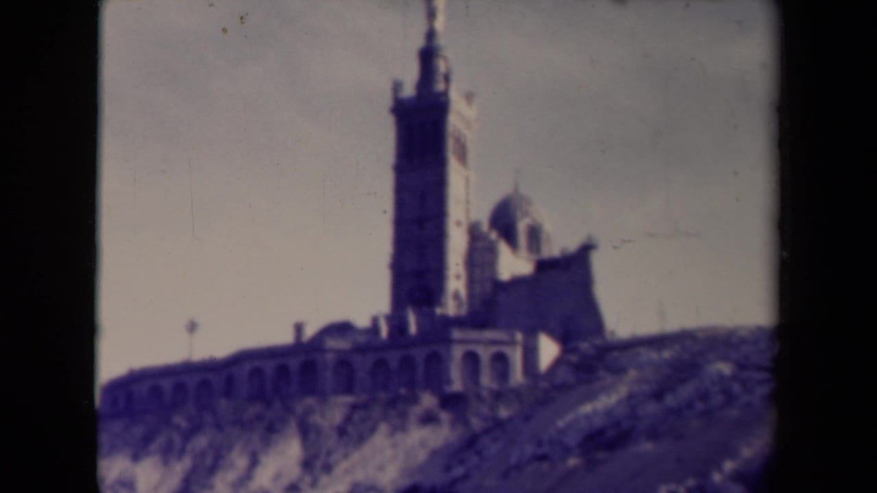 Tall tower and domed chapel above an arched wall on a hillside.