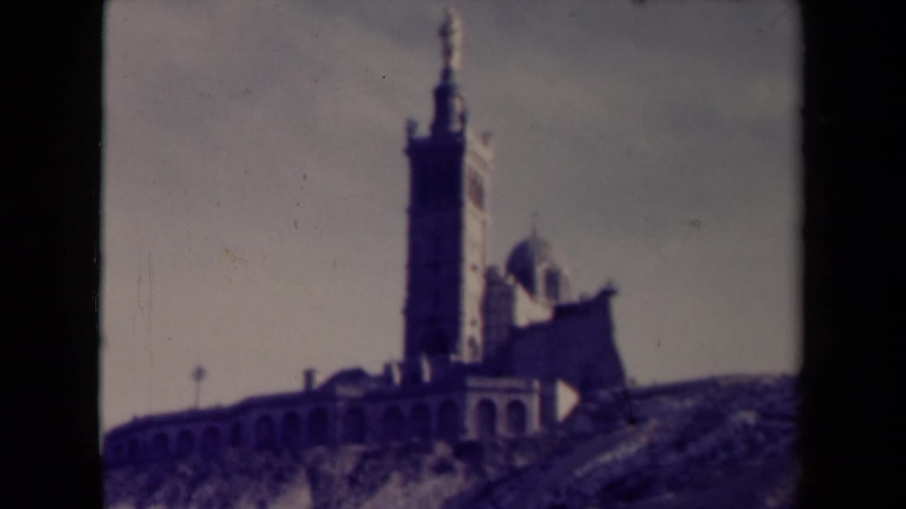 Hilltop religious complex with a tall tower, dome, and arched wall.