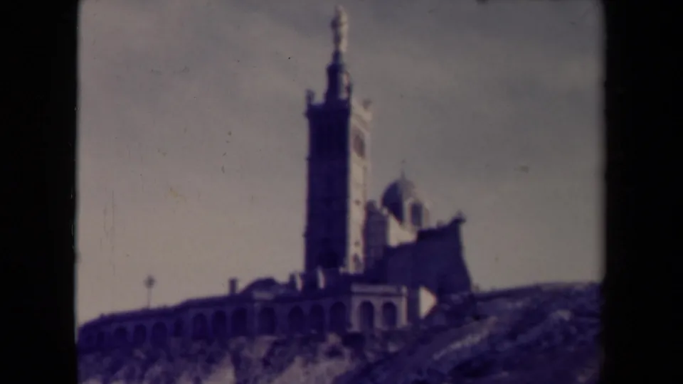 1945 France home-movie frame holding on the tower, chapel dome, and arched wall of a hilltop religious landmark.