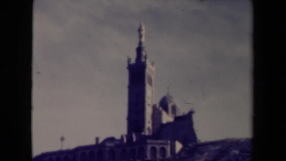 1945 France 8mm frame moving closer to a religious tower and domed chapel above a stone wall.