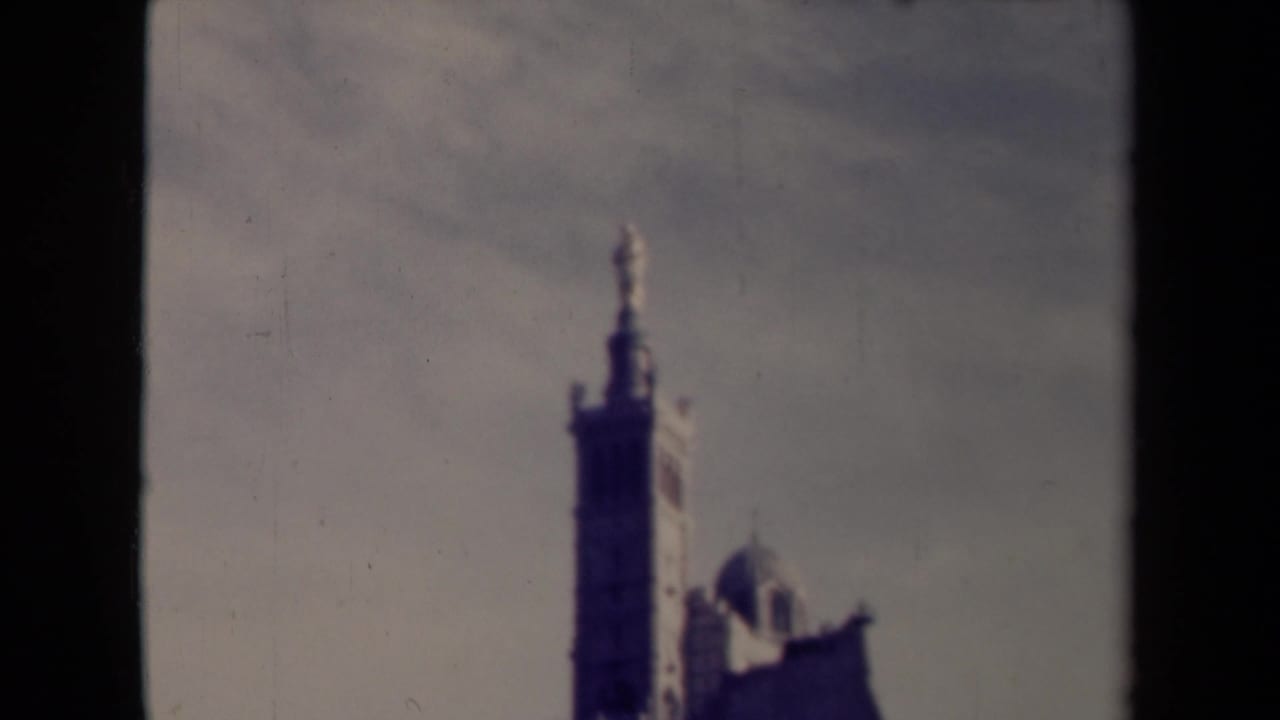 Soft, dark frame of a tall tower and roofline seen through 8mm film edges.