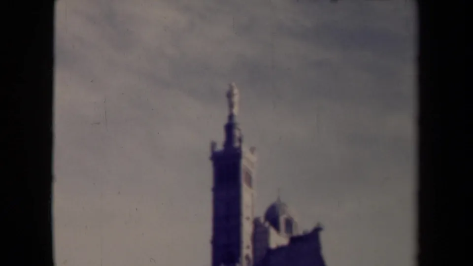 Faded 8mm frame from France showing a tall tower and partial domed roofline against a bright sky.