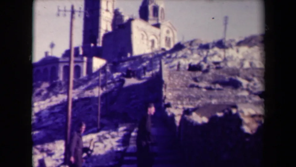 Two figures continue up the staircase beneath a towered historic-looking building in a faded France 8mm frame.