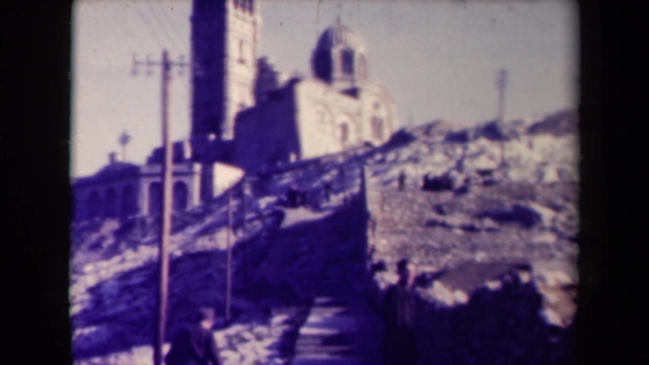 White church with bell tower on a rocky hillside beside steps and utility poles.