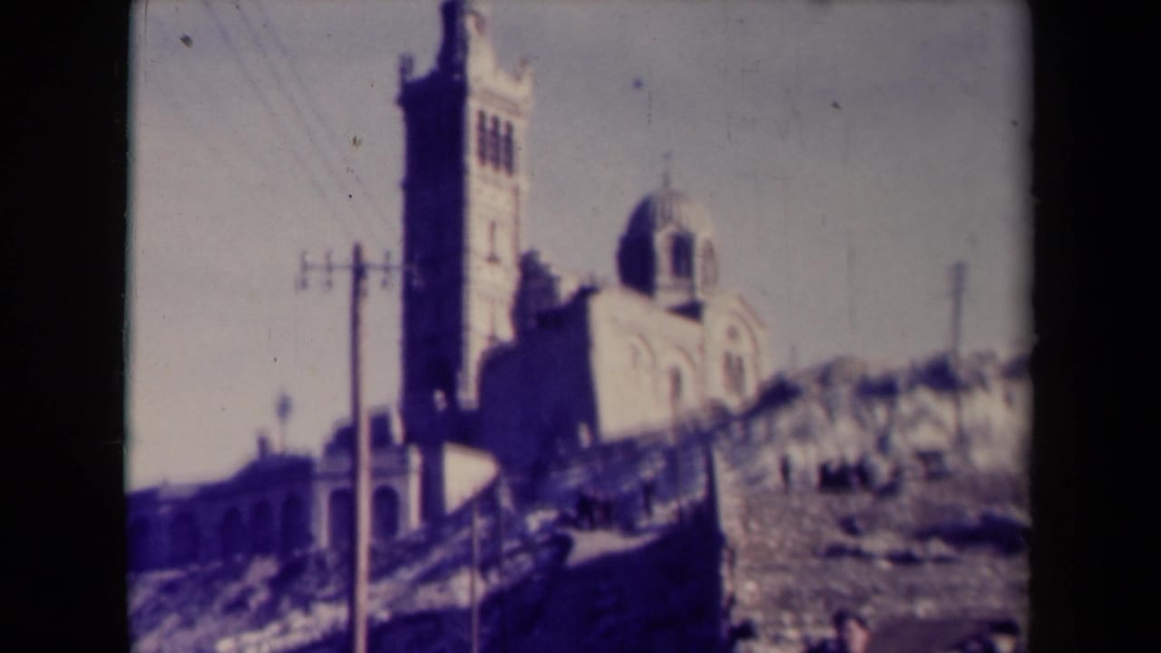 Vintage France travel frame showing the church from a slightly different angle, with utility poles and a rocky hillside in the foreground.