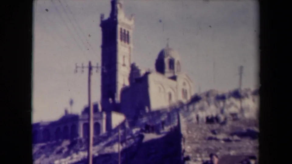 Vintage France travel frame showing the church from a slightly different angle, with utility poles and a rocky hillside in the foreground.