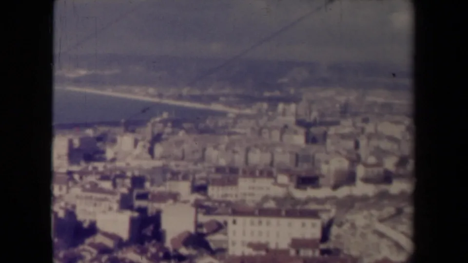 1945 France 8mm view across a dense urban area with pale facades, rooflines, waterfront infrastructure, and distant land across the water.