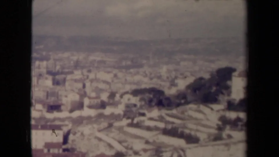 1945 France frame showing the pan reaching a brighter section of city, with dense buildings, waterfront distance, and terraced or hillside ground at the right.