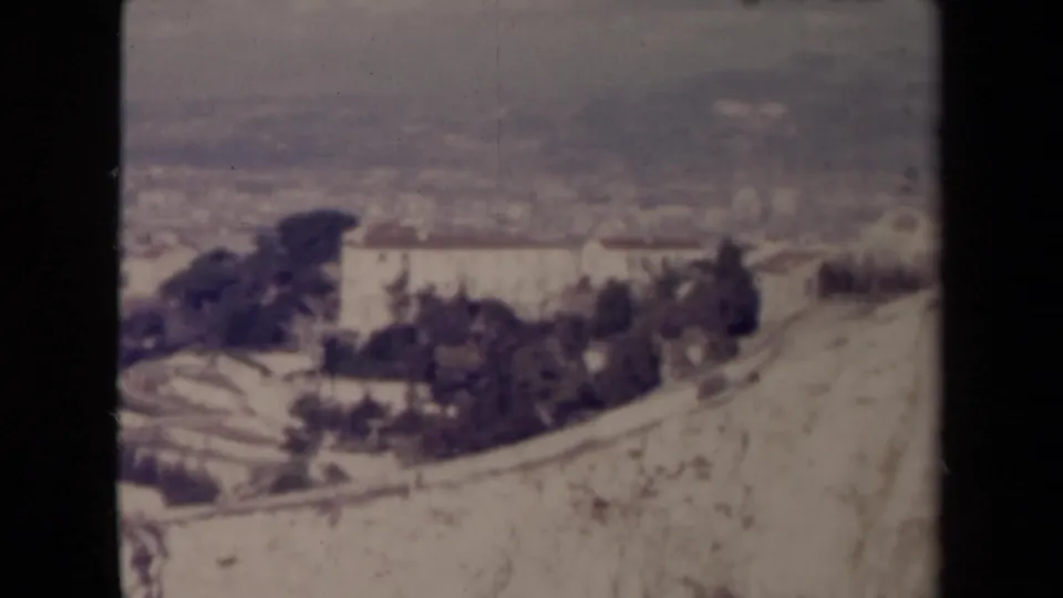 1940s France home-movie frame showing a soft elevated view over a hillside building, trees, and distant terrain.