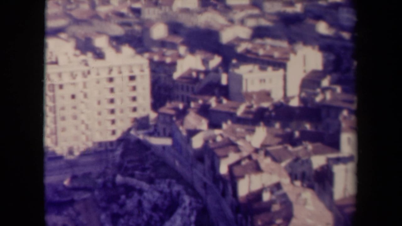 High-angle cityscape with a large pale building and dense roofs.