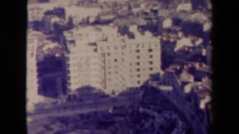 1940s France home-movie frame with an elevated view of a pale block, rooftops, and surrounding urban fabric.