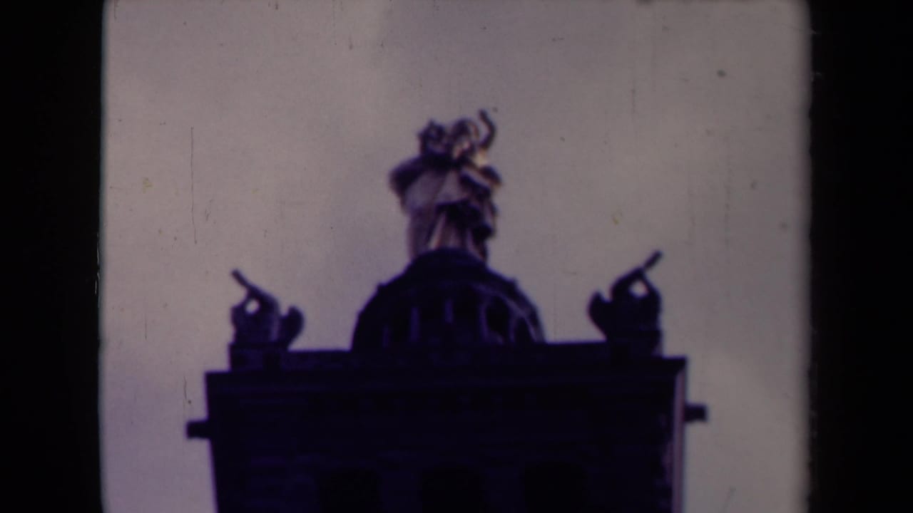 Low-angle view of rooftop statues and a domed architectural feature against a pale sky.